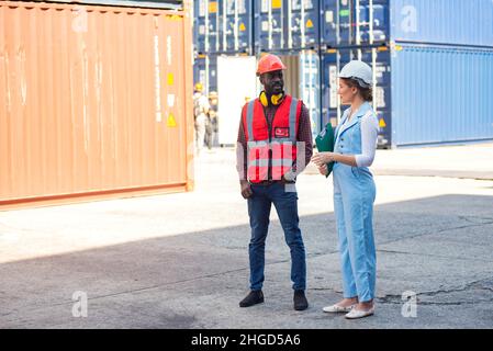 Businesswoman and engineer talking and checking loading Containers box from Cargo freight ship for import export. shipping in docks. Stock Photo