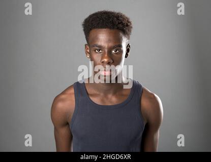 Confident muscular African American male in gray tank t shirt looking at camera with serious face on gray background in studio Stock Photo