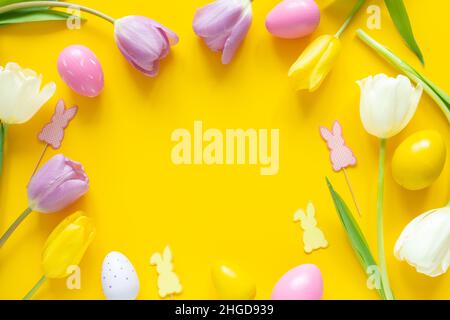 Greeting card with text. Multicolored easter eggs and tulips on yellow background. Copy space for your text Stock Photo