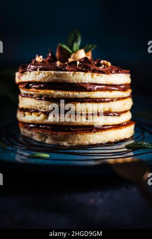 American pancakes with chocolate filling with mint and hazelnuts on a blue plate with dark background Stock Photo