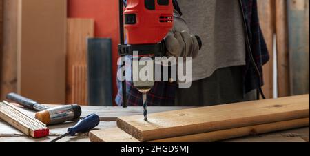 Drill electric tool, carpenter hand drilling wooden plank. Construction industry, work bench table closeup view Stock Photo