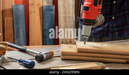 Drill electric tool, carpenter hand drilling wooden plank. Construction industry, work bench table closeup view Stock Photo