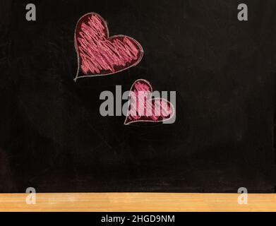 Heart drawing on school chalkboard. Love, valentine day symbol. Two red hearts small and big size hand drawn on black board Stock Photo