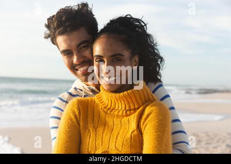 Portrait of smiling multiracial couple standing at beach against sky on sunny day Stock Photo