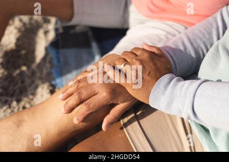 Midsection of biracial senior woman with hands on man's knee sitting at beach during sunny day Stock Photo