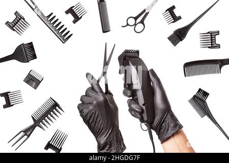Hairdressers hands in black rubber gloves holds hair clipper and scissors surrounded by professional hairdressing accessories. Isolated on white backg Stock Photo