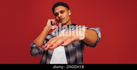 Flowing with the music. Young man enjoying his favourite playlist while standing against a red background. Handsome young man listening to music on wi Stock Photo