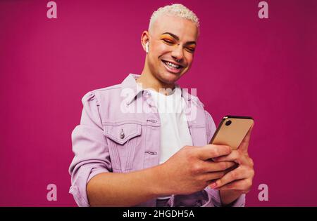 Enjoying contemporary music. Happy young man using a smartphone while wearing wireless earphones in a studio. Non-conforming queer man smiling cheerfu Stock Photo