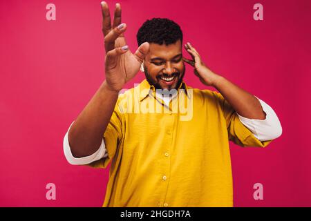 Streaming trendy music in the studio. Happy young man dancing cheerfully while listening to music using wireless earphones. Smiling young man standing Stock Photo