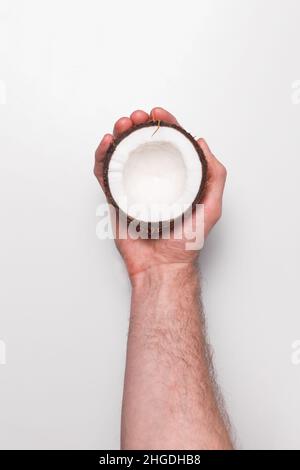 Coconut half in men's hand on white background. Top view Stock Photo