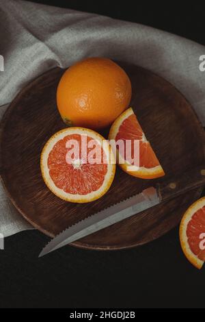 Moody Citrus Flat Lay Vertical. Cara Cara Oranges on Dark Background. Orange Slices on Wooden Plate. Dark Winter Aesthetic. Food Still Life. Stock Photo