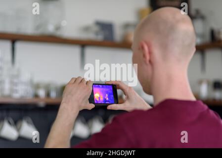 Person doing thermal scanning or imaging of apartment with smartphone app. Thermographic Inspection to check effectiveness of insulation Stock Photo