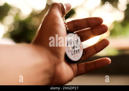 A man's hand holds a round keychain with the words Mixed with Love on a soft light background of the setting sun Stock Photo