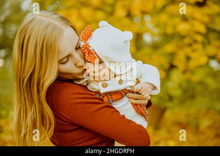 Happy joyful young family mom with little baby  girl having fun outdoors. Parents kiss their flying baby. Mother and daughter on autumn fallen leaves Stock Photo