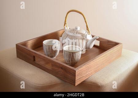 Ornate white gilt gold and brown teapot, raffia handle, with cups on a wooden tray Stock Photo