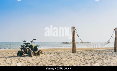 Vintage green ATV on the sandy beach. Quad ATV all terrain vehicle parked on beach, Motor bikes ready for action with summer sun flaring on bright day Stock Photo