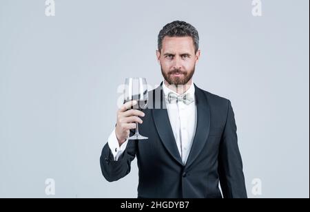 handsome tuxedo man cheers with glass of red wine hold gift box behind back, copy space, sommelier Stock Photo