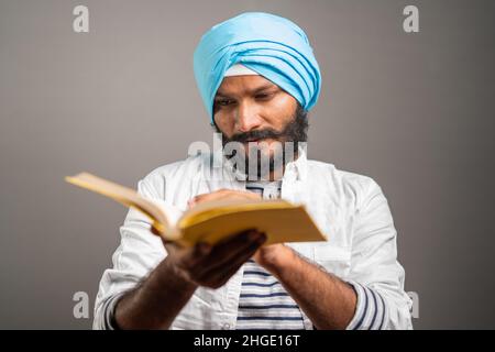 young sikh man reading holy religious Scripture for praying god on grey background - concept of spiritual belifes, worship and traditional culture. Stock Photo