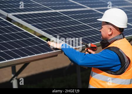 Solar power plant worker with electric wrench in his hands inspects panels Stock Photo