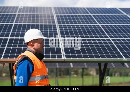 Engineer in work clothes and helmet walks through a solar power plant against the backdrop of panels Stock Photo