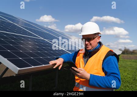 Man in hard hat using smartphone on the background of solar panels Stock Photo