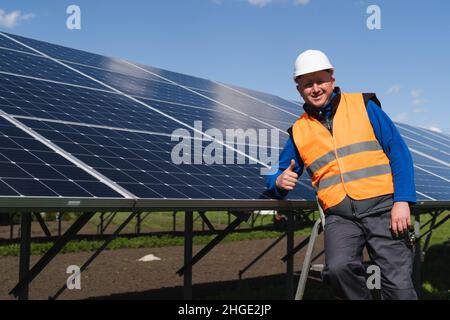 Satisfied worker showing thumb up gesture while standing near solar panels at power plant Stock Photo