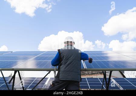 Back view of a man works with a drill screwdriver on solar panels Stock Photo