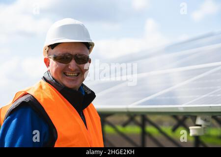 Close up portrait of engineer in a hard hat and protective glasses on a farm with solar panels Stock Photo