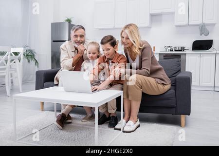 boy using laptop near smiling grandparents and sister in kitchen Stock Photo