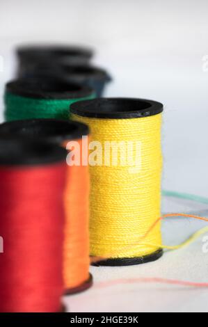 Spool of yellow tread with red and orange thread in foreground and green thread in background, white backdrop Stock Photo