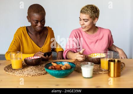 Happy multiethnic female couple relaxing at home while having breakfast Stock Photo