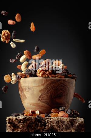 Flying dried fruits and nuts. The mix of nuts and raisins in a wooden bowl. Stock Photo