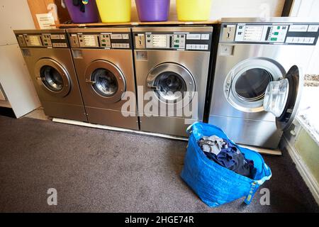 bag of clean laundry and open washing machine in row of washing machines in a launderette in ambleside lake district, cumbria, england, uk Stock Photo