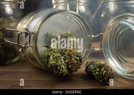 Dry CBD hemp buds, cannabis potheads spilled from a glass jar on the table. Stock Photo