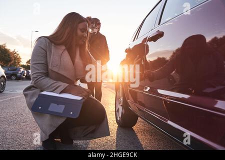 insurance agent examines the car while the driver talks on the mobile phone. Accident claim process. African-American woman checking the damage to the Stock Photo