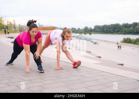 Professional fitness female trainer have personal training with positive overweight young woman outdoor in summer morning. Stock Photo