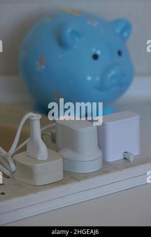 Close up of a multiple electric socket with plugs and a blurred piggy bank. Stock Photo