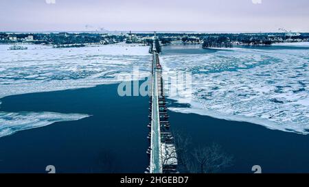 The frozen landscape with hiking/walking trail bridge over the frozen water. The trestle (friendship) trail extends to another city over the lake. Stock Photo