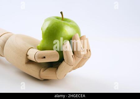 A wooden hand holding a bitten granny smith apple on a white background. Stock Photo