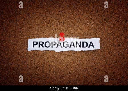 A piece of paper with the word Propaganda written on it that is pinned to a cork board. Close up Stock Photo