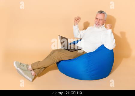 Portrait of handsome trendy cheery lucky man using laptop rejoicing isolated on beige pastel color background Stock Photo