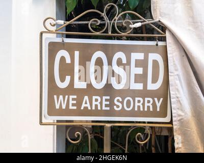 Metal sign saying: Closed. We are sorry. On brown background. Stock Photo