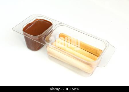 Chocolate cream in transparent plastic container. Sweet wafer sticks and brown hazelnut cream isolated on white Stock Photo