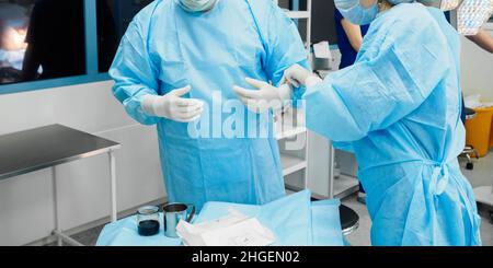 Surgeons in blue uniforms wear sterile gloves before surgery. Stock Photo