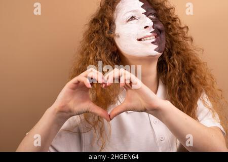 A beautiful girl with red hair and blue eyes painted with the Qatar flag on her face shows a heart with her hands. Isolated on a brown background Stock Photo