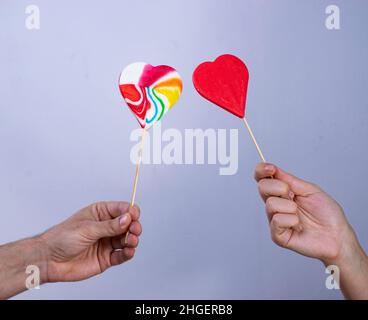 A woman's and a man's hand hold two lollipops in the shape of a heart. Stock Photo