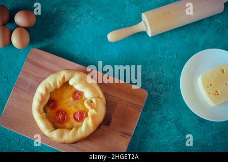 Deep Dish Pizza. Сhicago pizza 4 cheeses, dried cherry tomatoes. Food on a wooden plate, rolling pin and 4 eggs, piece of cheese, ingredients.. Pastry Stock Photo