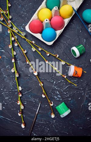 Happy Easter. Colored eggs in a carton eggs. Flowering willow fur seal, on an abstract background of dark color. Multicolored paints, brushes, waterco Stock Photo