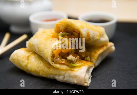 Close-up of some homemade spring rolls on a black slate plate with soy sauce, sweet and sour and some Chinese wooden chopsticks Stock Photo