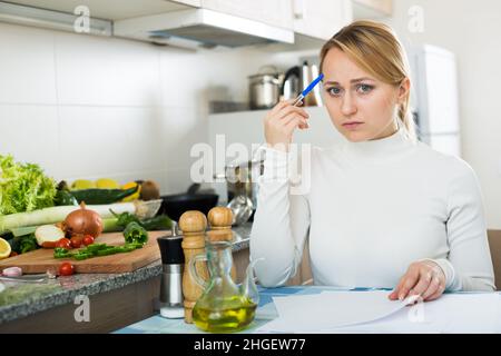 Sad housewife with documents in kitchen Stock Photo